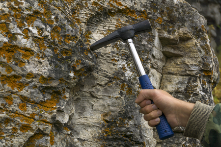 geologist's hand strikes a limestone mossy rock with a geological hammer to take a sampleの写真素材