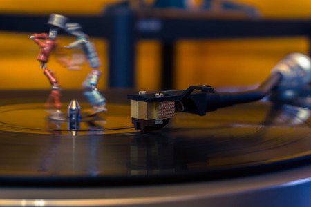 two funny small human figures, roughly welded together from resistors and transistors, dance on a rotating vinyl record in twilightの写真素材