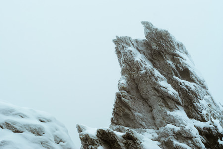 snow-covered frosty beautiful rock on top of a mountain during a snowfall in winter fogの写真素材