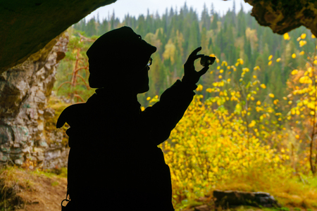 silhouette of a geologist examining a mineral sample found in a cave, on the background of an entrance with a brightly lit autumn forestの写真素材