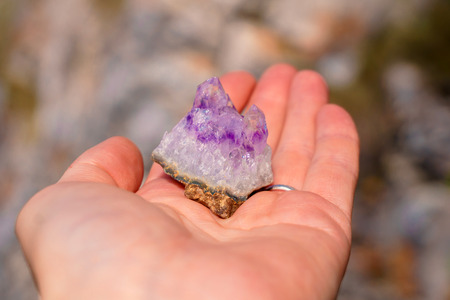 druse of natural untreated violet crystals of amethyst on a piece of rock lies on the palm of your...