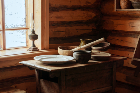 fragment of the interior of an old peasant log cabin - a table with wooden and ceramic dishes, a kerosene lampの写真素材