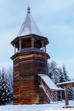 ancient wooden bell tower of russian village church in winter landscapeの写真素材