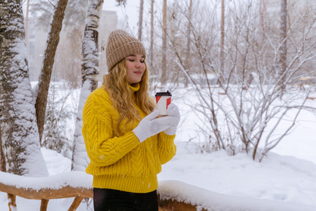 girl in a sweater holding a paper cup with a hot drink in a winter parkの写真素材