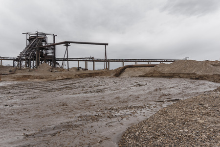 rusty pipe on the river bank, from which sewage flows, dirty sand slurry, and stationary rusty...