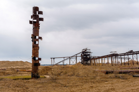 desert industrial landscape with stationary rusty gravitational separator of sand and gravel, strange rusty pipe resembling a totem pole on the foregroundの写真素材