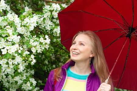 laughing young blond woman under a red umbrella against a blooming apple treeの写真素材