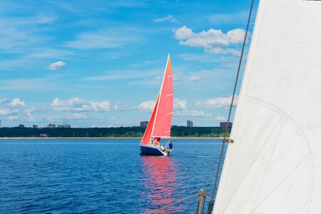four men are sailing on a sailboat with red sails on the lake against the backdrop of the shore with...