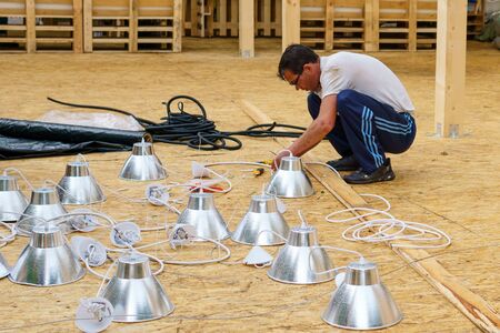 Perm, Russia - July 13, 2019: electrician assembles a lighting system sitting on the floor in a...