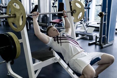 young man prepares to do the exercise barbell bench press from the chest in the gym