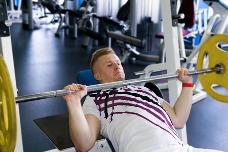 young man performs an exercise barbell bench press from the chest in the gym