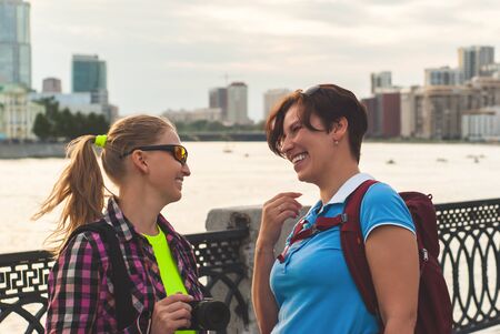 two women tourists talking and laughing on the promenade against the background of the river and the...