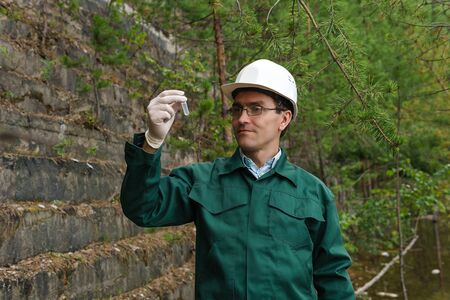 industrial ecologist or hydrologist takes a sample of water from old quarry
