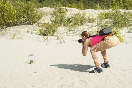 backstage - woman photographer at work outdoors shoots a toy house in the sandの写真素材
