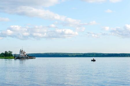wide summer river with a fishermanâs boat and a tugboat near the shoreの写真素材