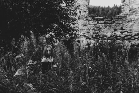 monochrome gloomy view of the ruins and woman of a zombie or witch among tall grassの写真素材