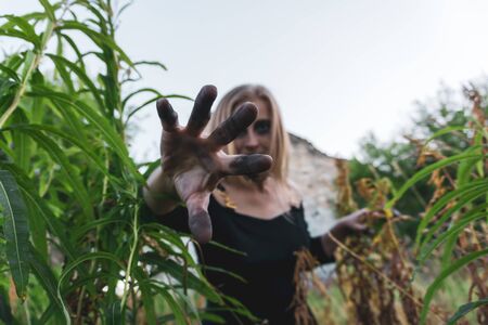 young woman cosplaying a scary witch stretches her hand with black fingers into the frameの写真素材
