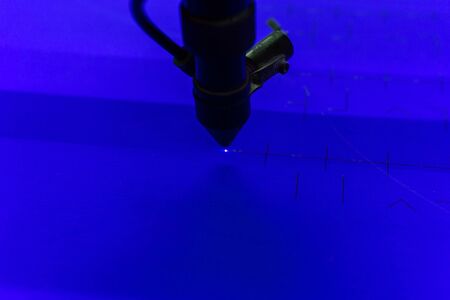 close-up of a flying head of a laser cutting machine, beam burning out grooves in blue sheet...