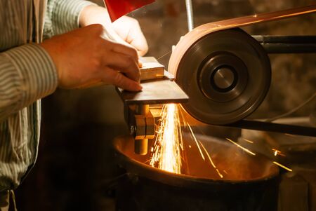 the hands of a locksmith grinding the workpiece for a knife on a grinding belt