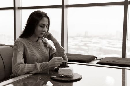 young woman sitting at a table in a cafe stirs sugar in coffeeの写真素材