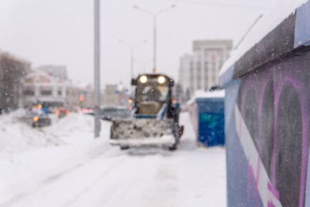 blurred background - city during snowfall, visible outline of a snowplow riding on the sidewalkの写真素材