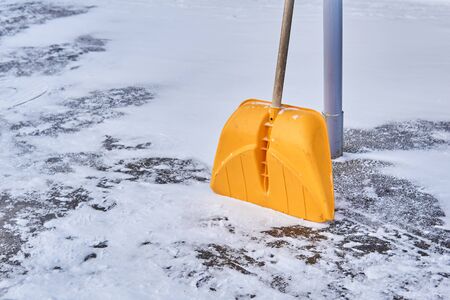 yellow plastic snow shovel leaning against a pole on a snowy pavement
