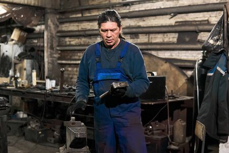 aged male blacksmith chooses a hammer to start working in a workshop getting ready for work