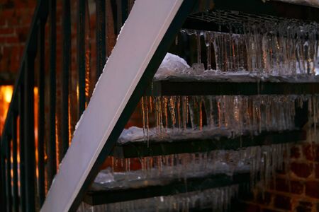 winter background - outdoor staircase at evening twilight covered with ice and icicles lit by a window behind itの写真素材