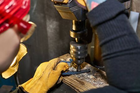 female artisan doing machining of metal artwork on a drilling machine with countersink cutter, focus...