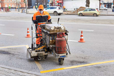 Perm, Russia - April 27, 2020: worker update markup at the bus stop using a road marking machine