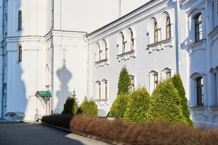 courtyard of an old orthodox monastery with junipers and a shadow from a church dome on a white wall