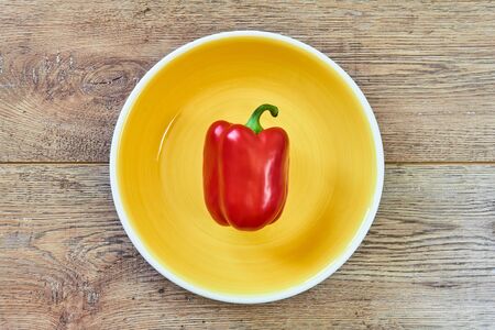 color still life - red bell pepper on a yellow plate on a wooden tabletopの写真素材