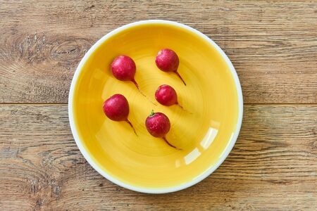 color still life - five red radishes as if moving on a yellow plate on a wooden tabletopの写真素材