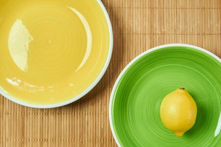 color still life - lemon on a green plate next to a yellow empty plate on a cane tableclothの写真素材