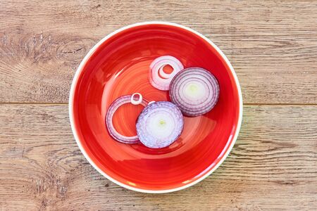 color still life - bulb of sweet purple onion sliced in rings on a red plate on a wooden tabletopの写真素材