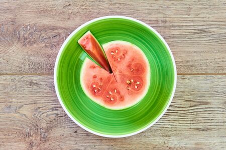 color still life - small ripe cut watermelon on a green plate on a wooden tabletopの写真素材