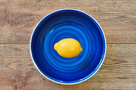 contrast still life - bright yellow lemon on a blue plate on a wooden tabletopの写真素材