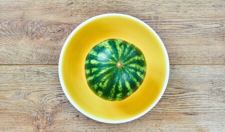 color still life - small watermelon on a yellow plate on a wooden tabletopの写真素材
