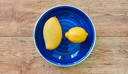 yellow fruits - lemon and mango - on a blue plate on a wooden tabletopの写真素材