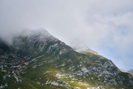 alpine landscape - the tops of the peaks are hidden by clouds through which the sun shines