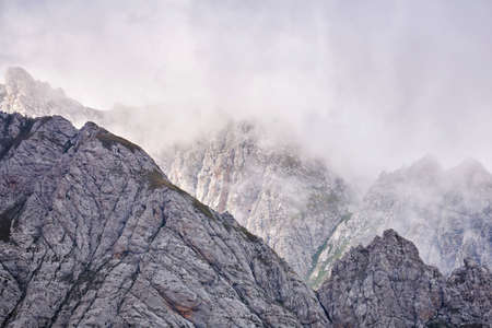 alpine landscape - sharp rocky mountain peaks hide in the clouds