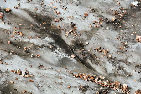 muddy surface of a melting mountain glacier covered with rocks and rubble