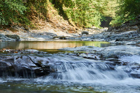 cascade of small waterfalls and pools on a mountain stream in a wooded gorge