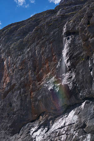 sheer cliff and a small waterfall with rainbow against the skyの写真素材