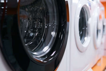 row of washing machines for sale in a home appliance store, close-up with blurred background