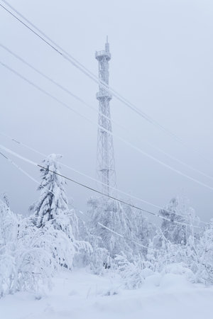 ice-covered cell tower over a snowy forest on top of a mountain against a winter skyの写真素材