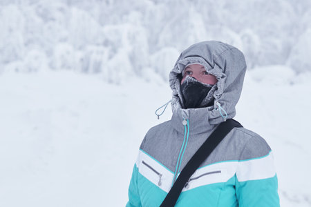 young woman in a warm jacket with a hood and a buff neck gaiter on her face against the background...