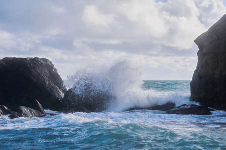 stormy surf with splashes among coastal rocks on the shore of the winter seaの写真素材