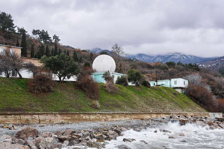 small observatory with a white geodesic dome on the seashore against the backdrop of mountains