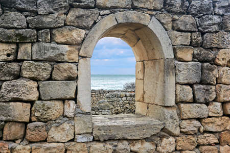 semicircular window opening in the ruins of an antique wall, behind which you can see the seaの写真素材